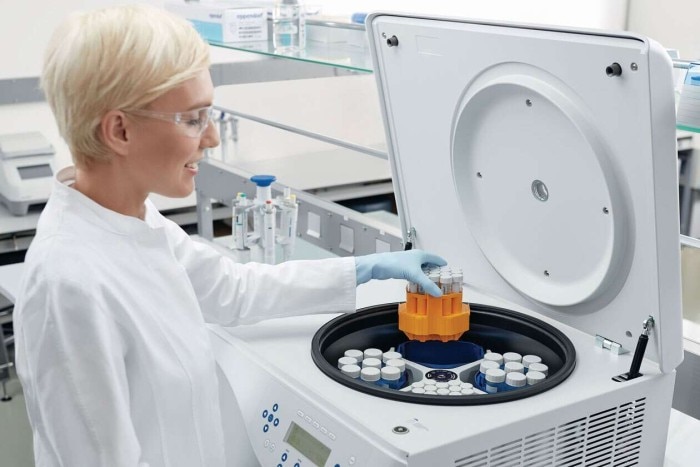 A scientist is putting some sample vessels with the label `Eppendorf´ into a centrifuge.