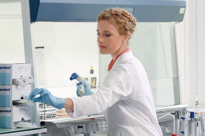 Scientist sitting at a safety cabinet in a laboratory using some Eppendorf packaging boxes.