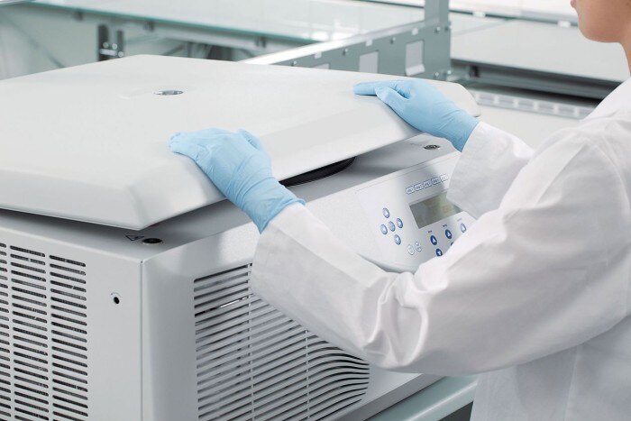 A lab worker is closing the centrifuge lid in the laboratory.