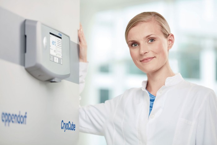 Female scientist stands next to an Ultra Low Temperature (ULT) freezer with the control display conveniently at eye level.