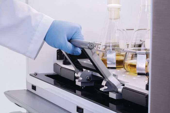 Scientist pulls out a shaker platform with heavy sample flasks, supported by an ergonomic design.