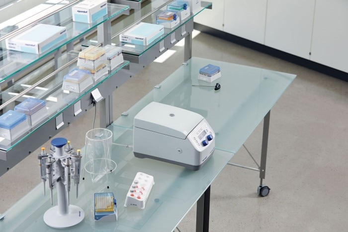 A benchtop centrifuge next to a pipette carousel in an ergonomically designed laboratory.