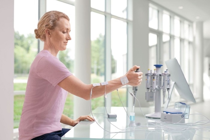 A scientist sits at the bench and is connected with electrodes at the arm to test muscle tension while using an Eppendorf pipette.