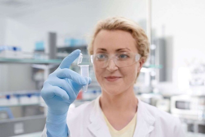 A female scientist in the laboratory checks a conical tube that she has in her hand.