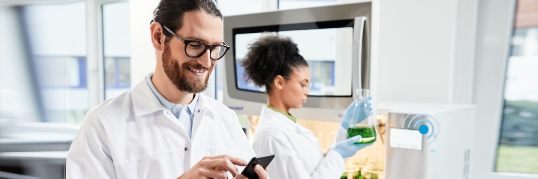 Man in the laboratory using a mobile phone to remotely monitor the performance of the biological shaker S44i with VisioNize.